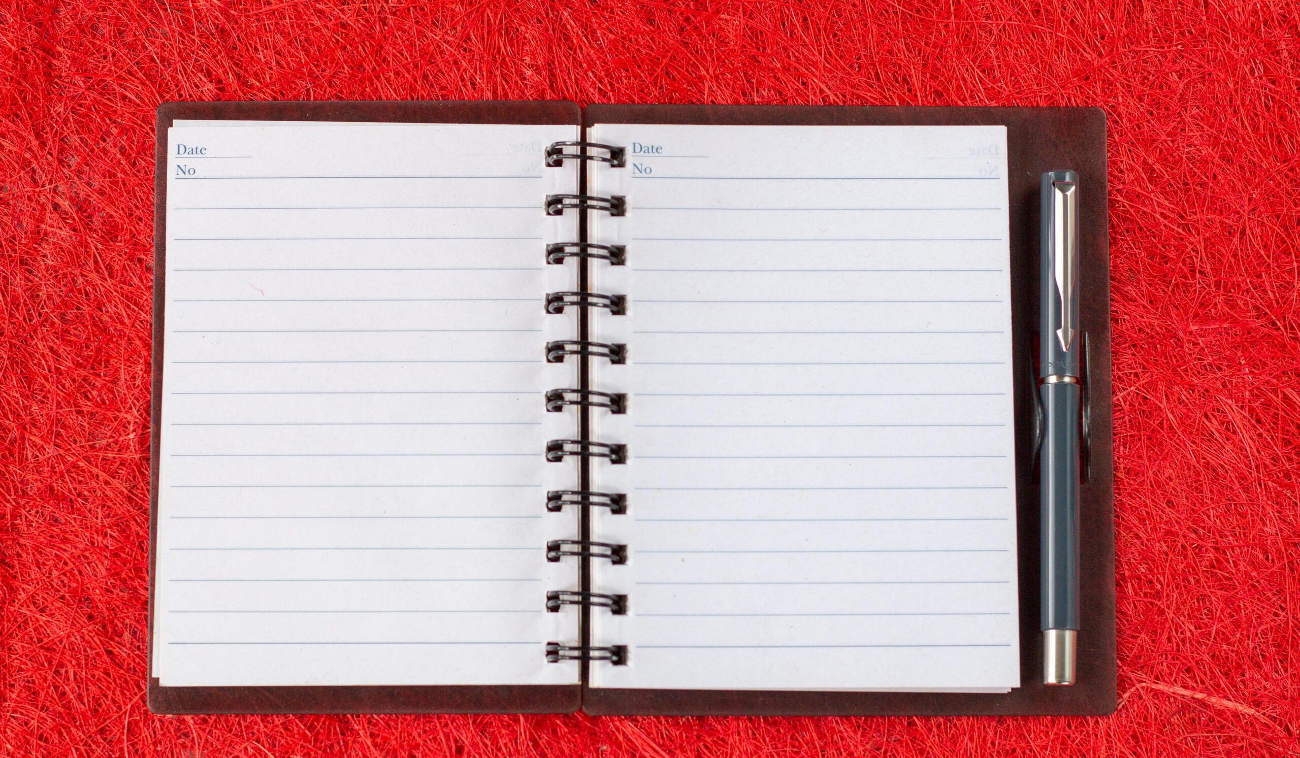 A photo of an open notebook and pen over a red background.